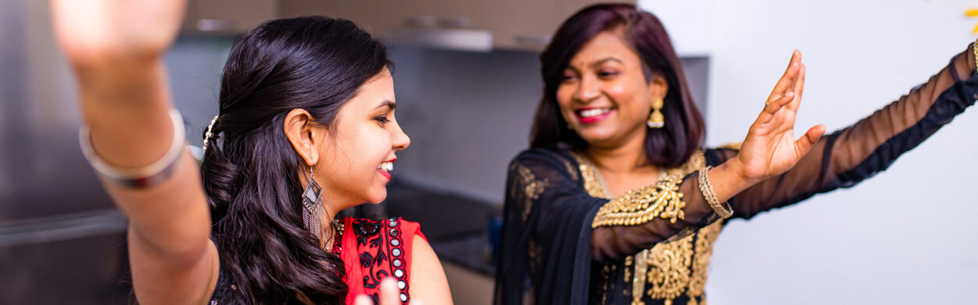 two women in black and gold and red sarees dancing in the kitchen