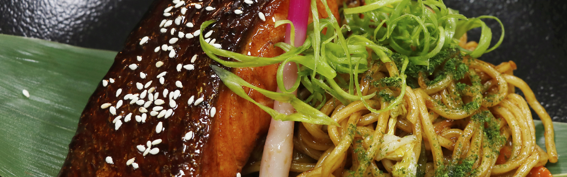 Main image: sticky salmon noodles, an easy salmon dinner recipe you can make at home. Sticky glazed salmon with veggie packed noodles on a large leaf. 