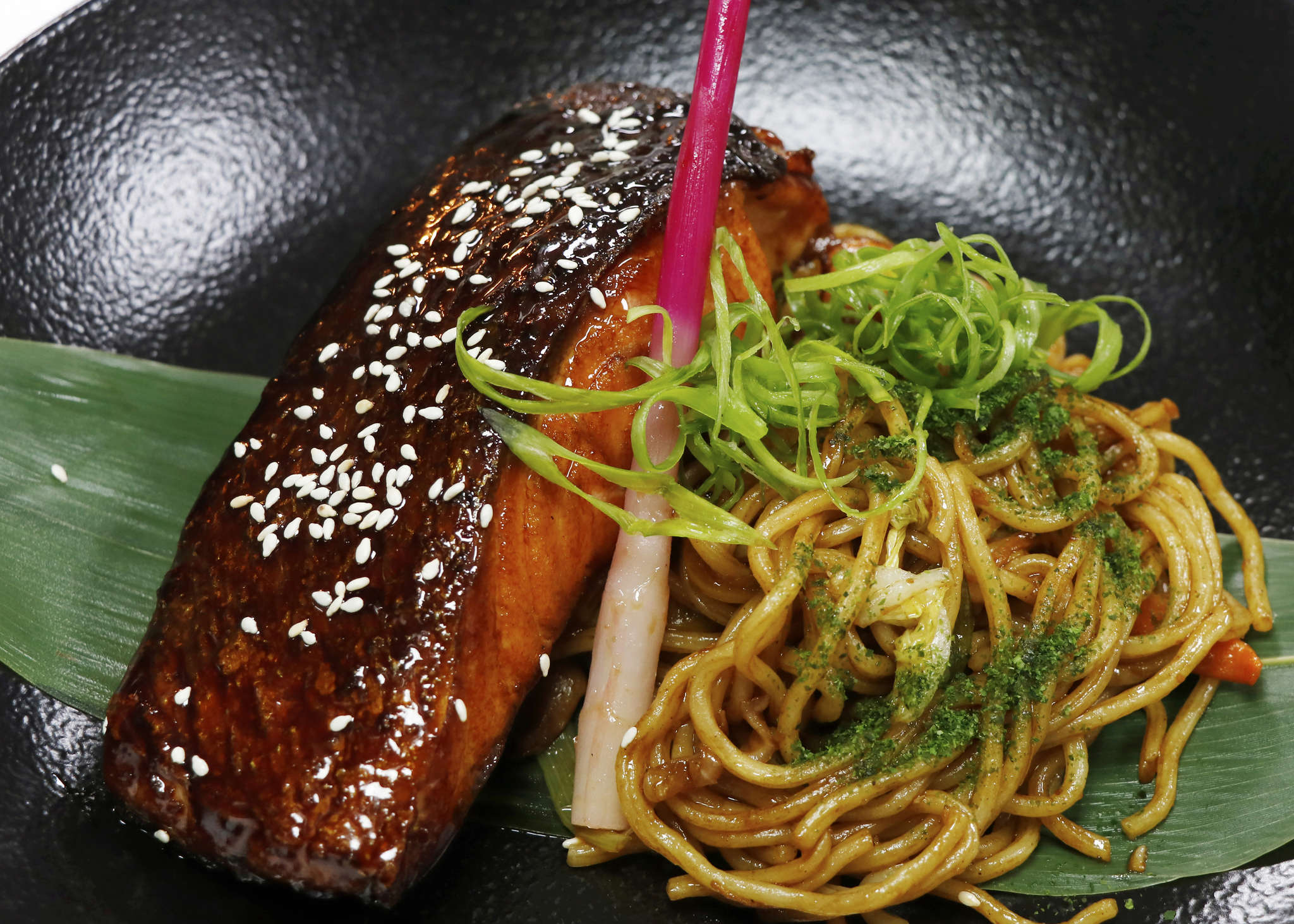 Main image: sticky salmon noodles, an easy salmon dinner recipe you can make at home. Sticky glazed salmon with veggie packed noodles on a large leaf. 