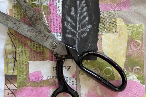 a pair of black steel scissors resting on a colourful collage