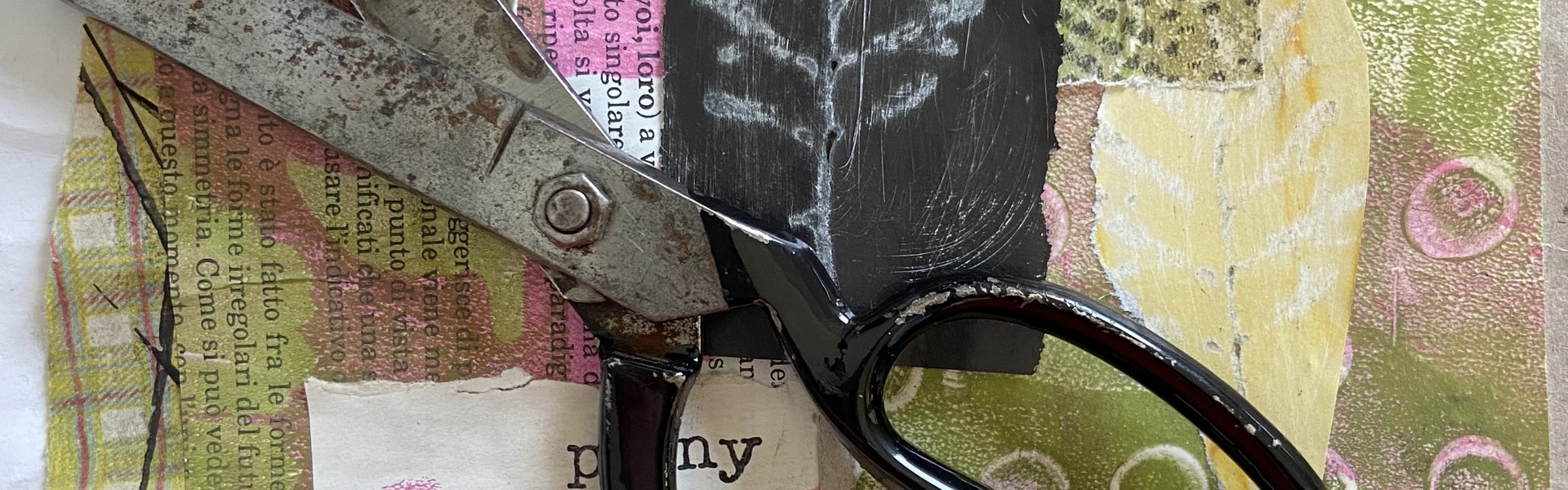 a pair of black steel scissors resting on a colourful collage