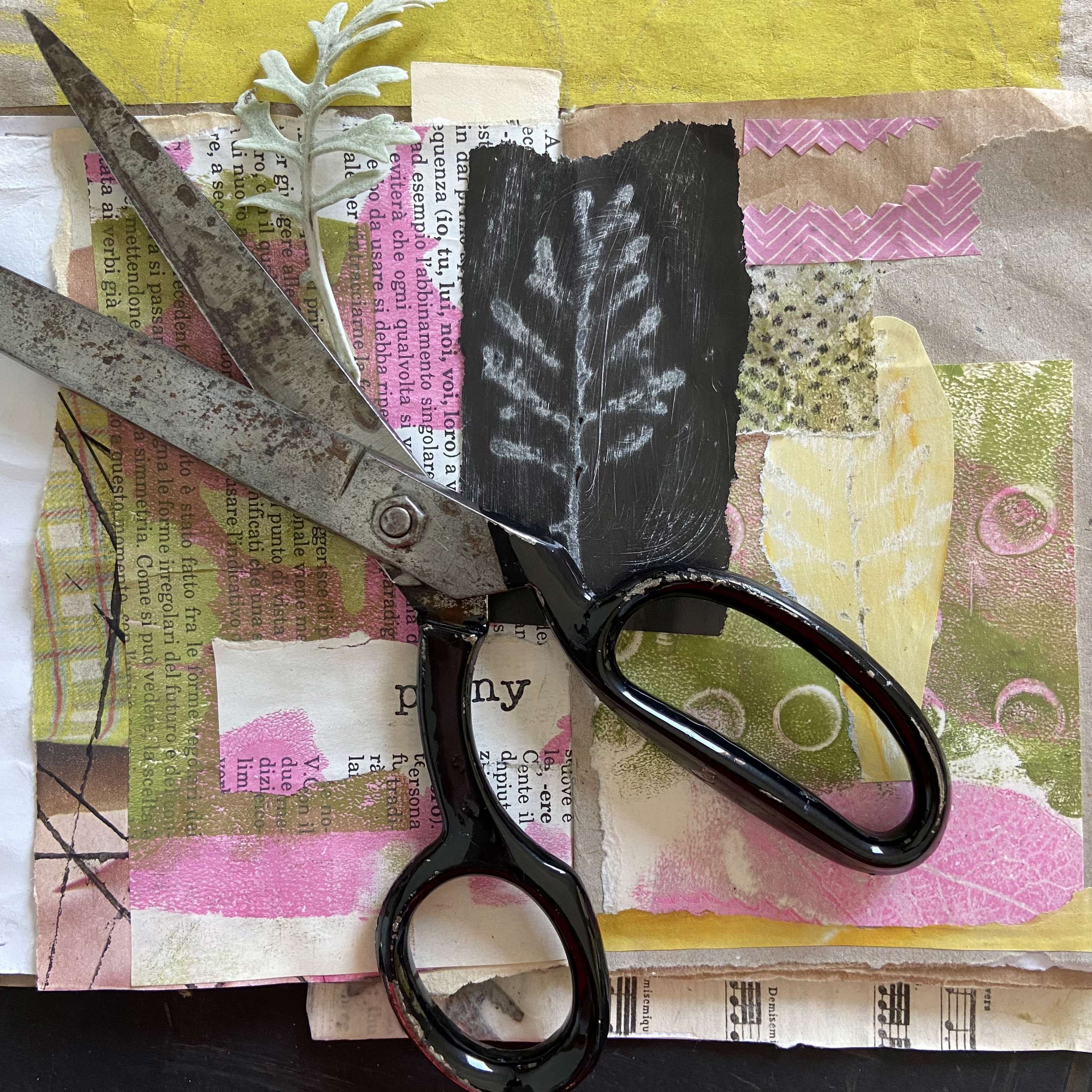 a pair of black steel scissors resting on a colourful collage