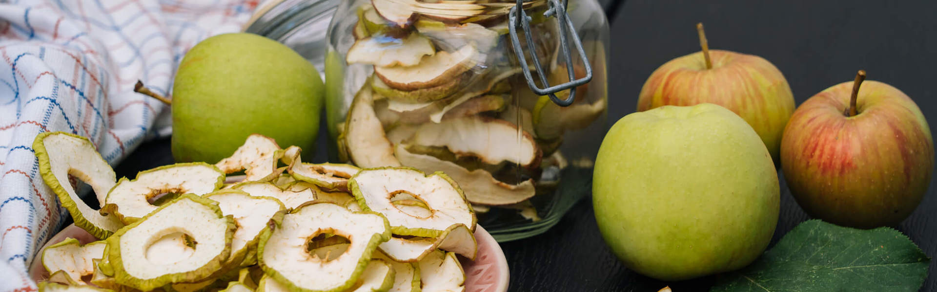 Main Image: dried apple rings, dried at home, in a jar and on plate, with fresh apples sat next to them on a table.