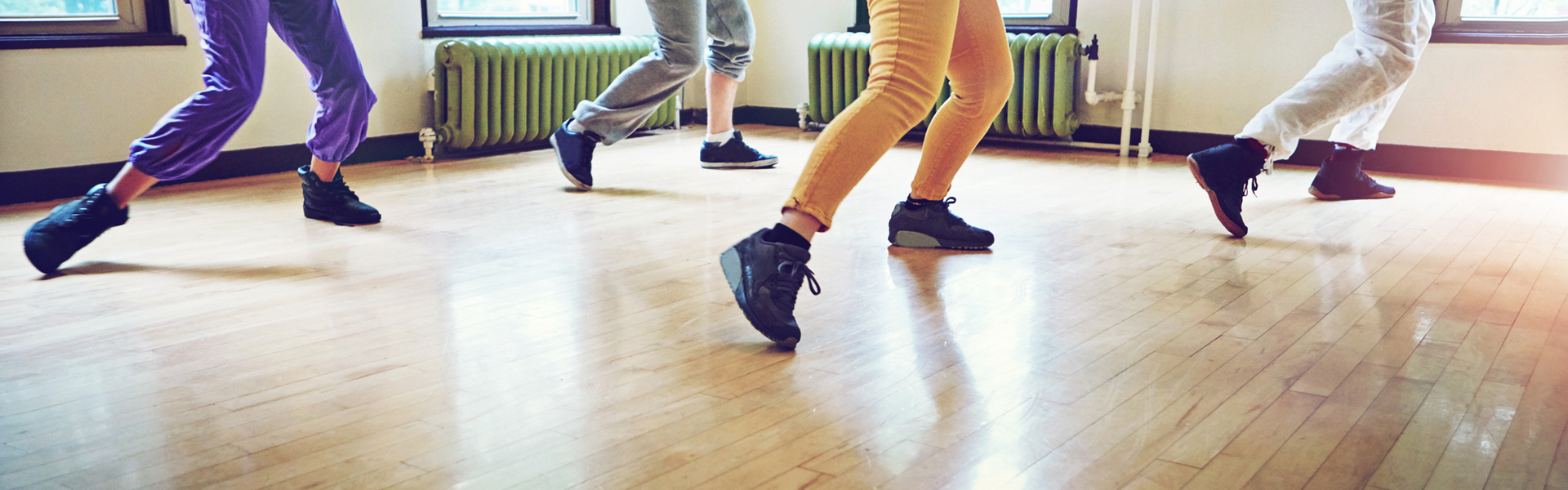 Photo of 4 people dancing in a class, with the image cut off at their shoulders.