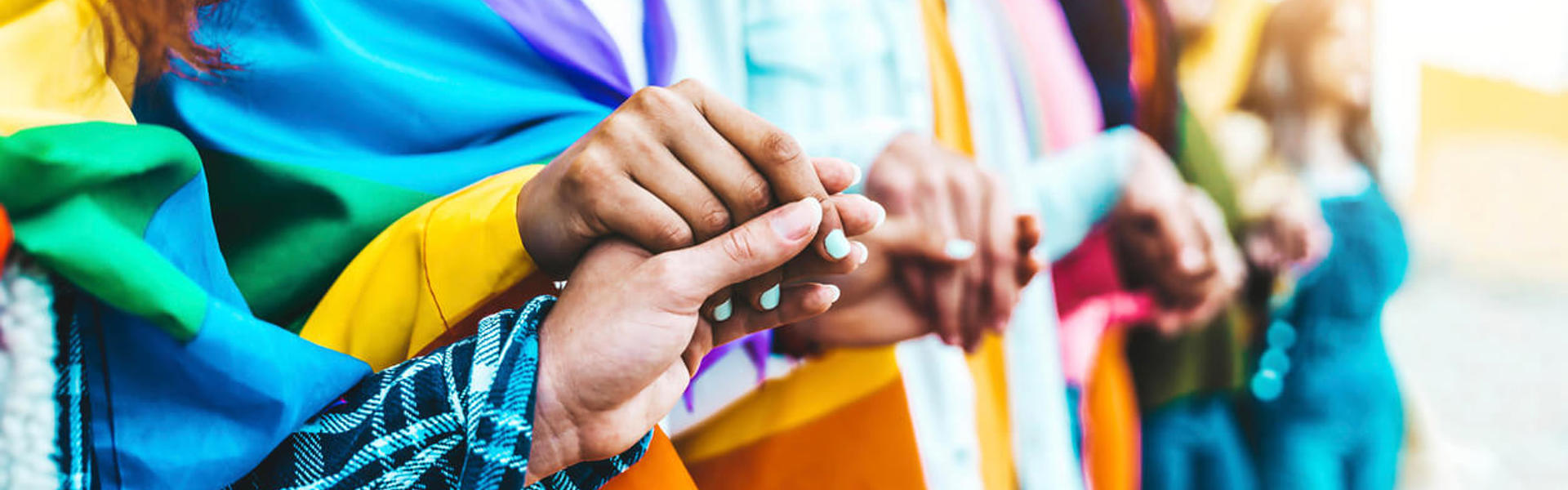 A diverse group of people holding hands, proudly displaying colourful rainbow flags in a show of unity and support.