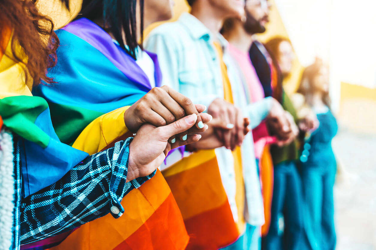 A diverse group of people holding hands, proudly displaying colourful rainbow flags in a show of unity and support.