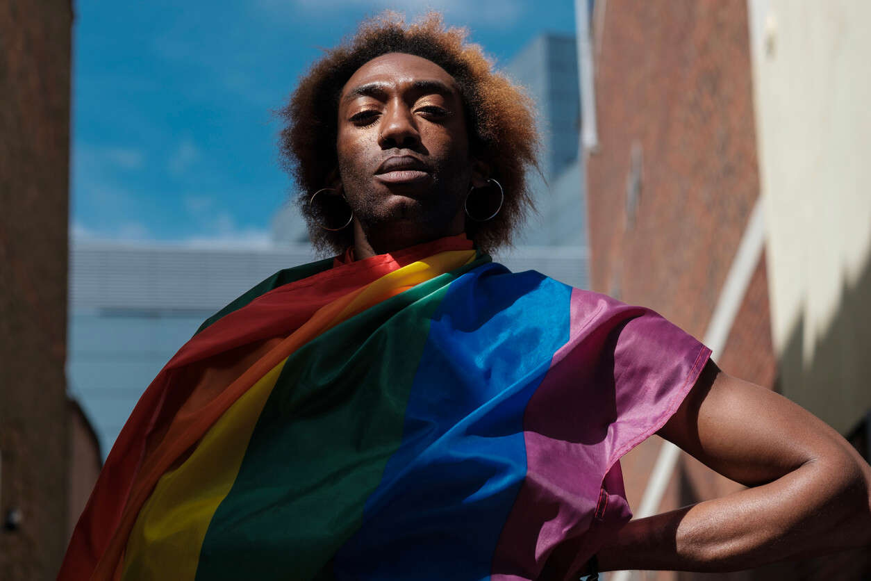 A serious non-binary young person is holding a lgbtq flag in a street of London