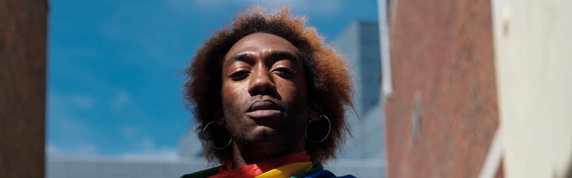 A serious non-binary young person is holding a lgbtq flag in a street of London