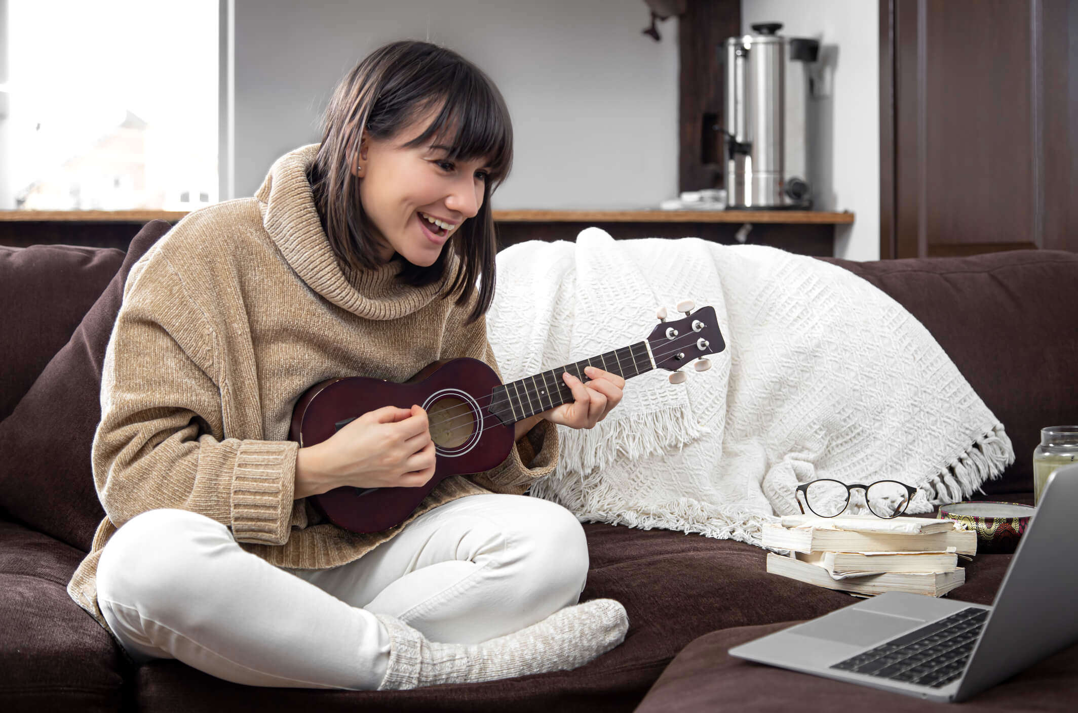 a woman sat on the sofa learning to play the ukulele from her laptop