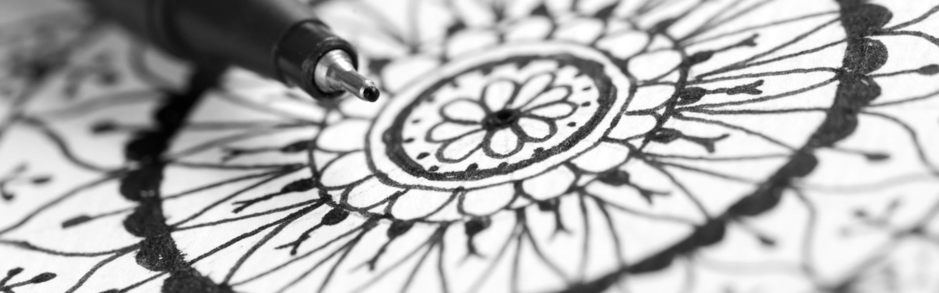 a close up of a ballpoint pen drawing a black mandala on white paper