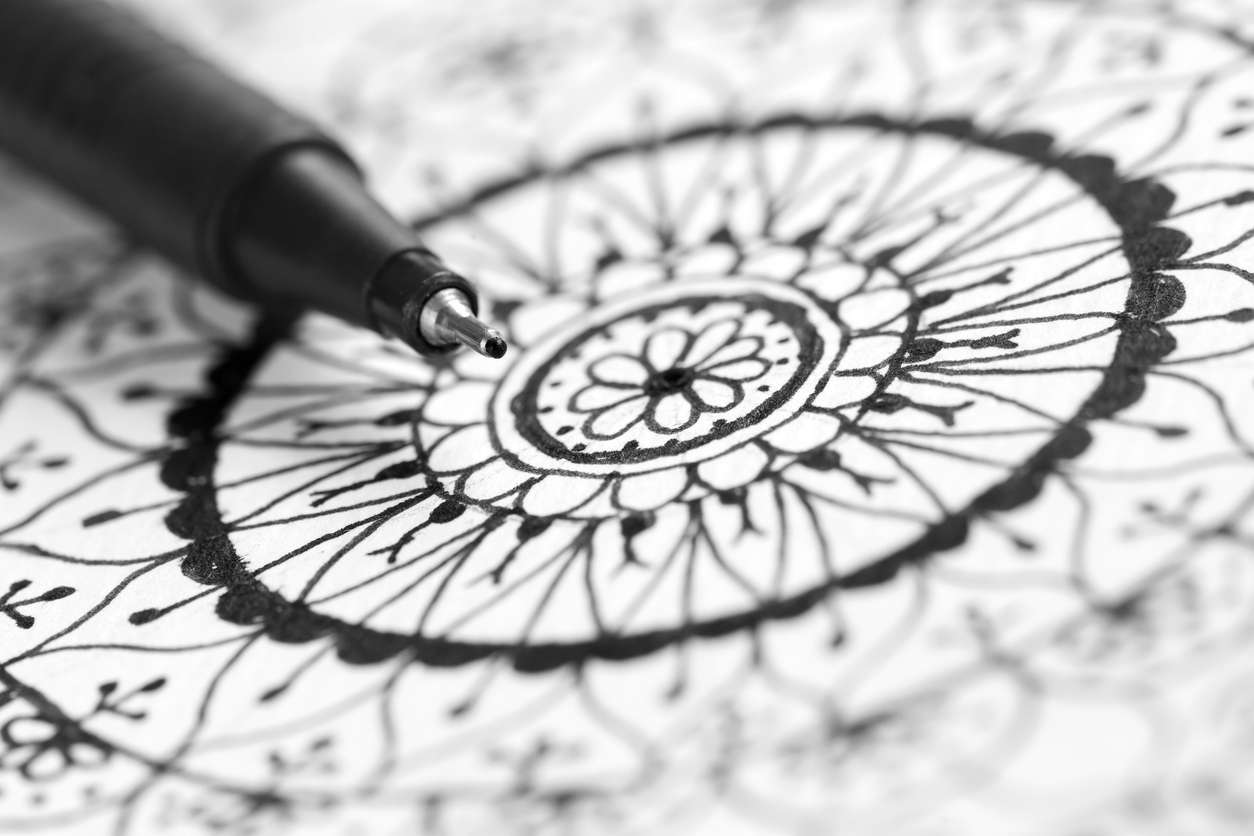 a close up of a ballpoint pen drawing a black mandala on white paper