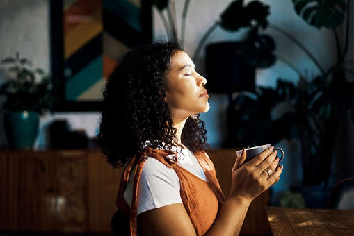 a woman holding a mug of tea facing the window and closing her eyes