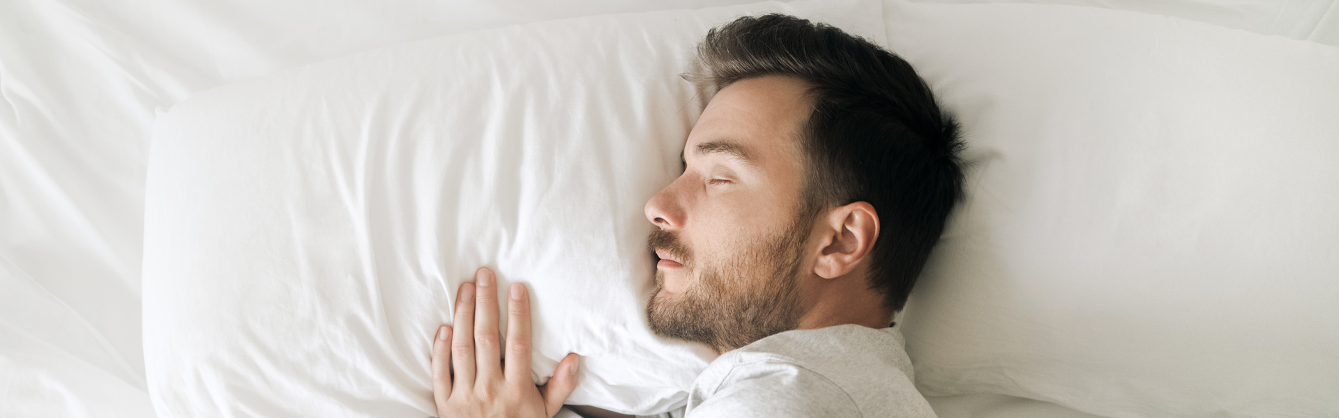 a man resting his head on a pillow in bed in white sheets sleeping