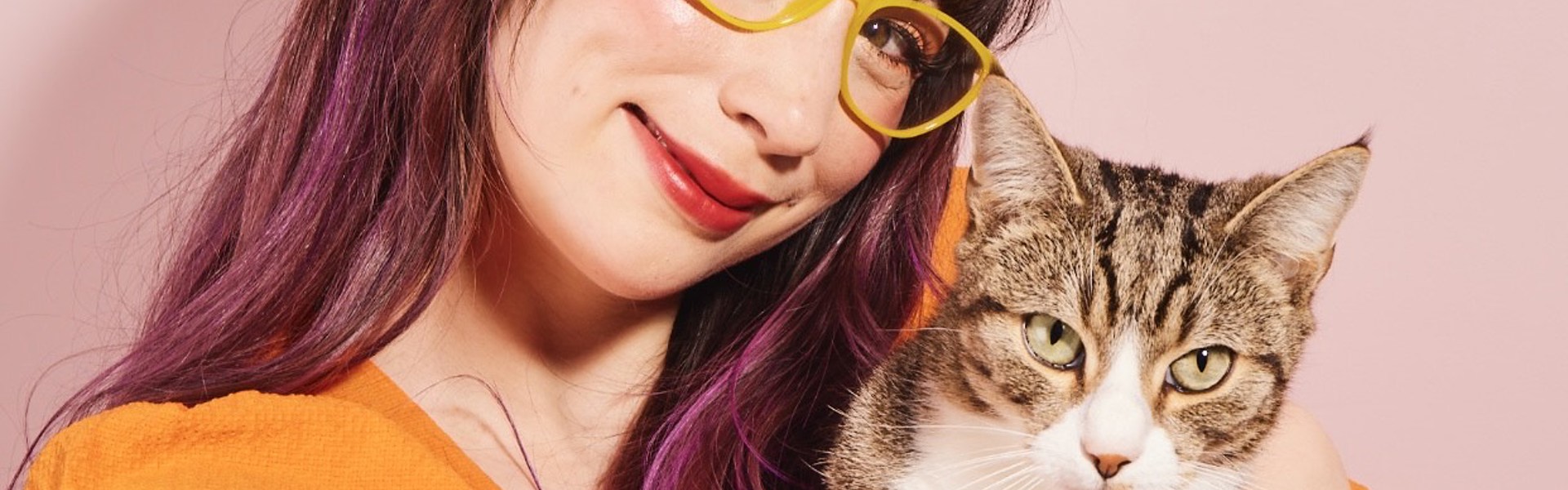 Main image: a photo of Kim Joy Author Of Ordinary Joy, cuddling her cat, wearing an orange top in front of a pink background.