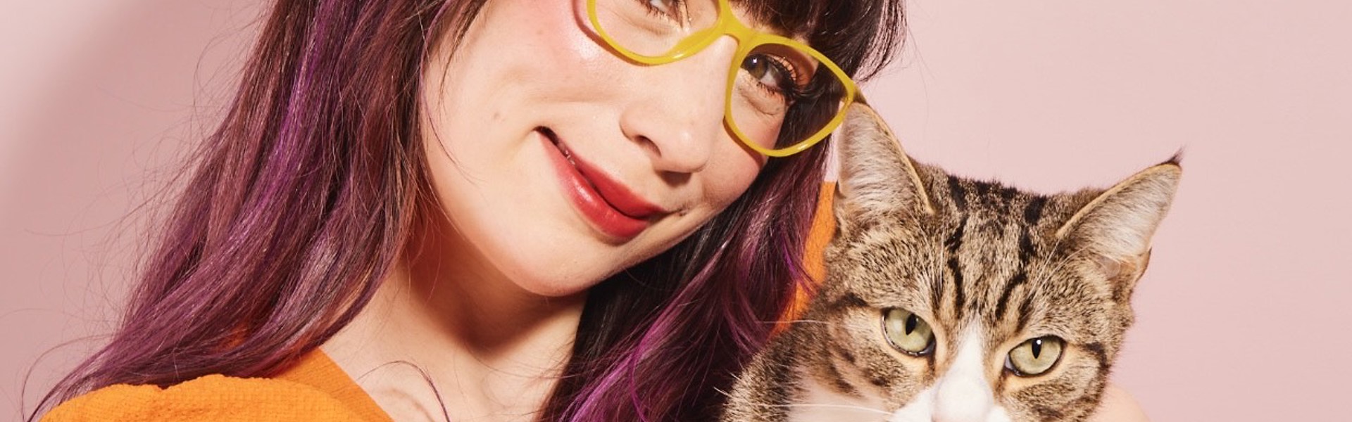 Main image: a photo of Kim Joy Author Of Ordinary Joy, cuddling her cat, wearing an orange top in front of a pink background.