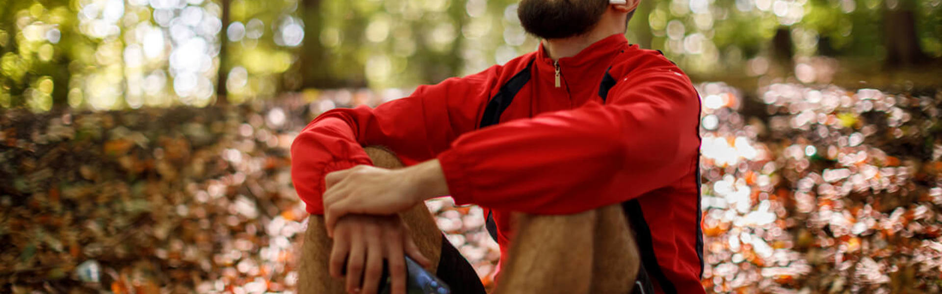 a man in a red jumper sat in the forest relaxing with headphones in and eyes closed