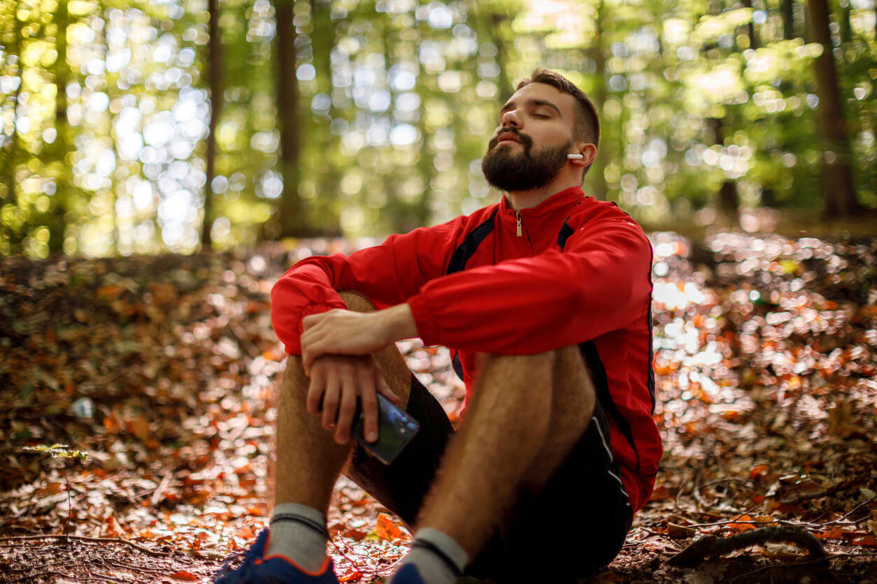 a man in a red jumper sat in the forest relaxing with headphones in and eyes closed