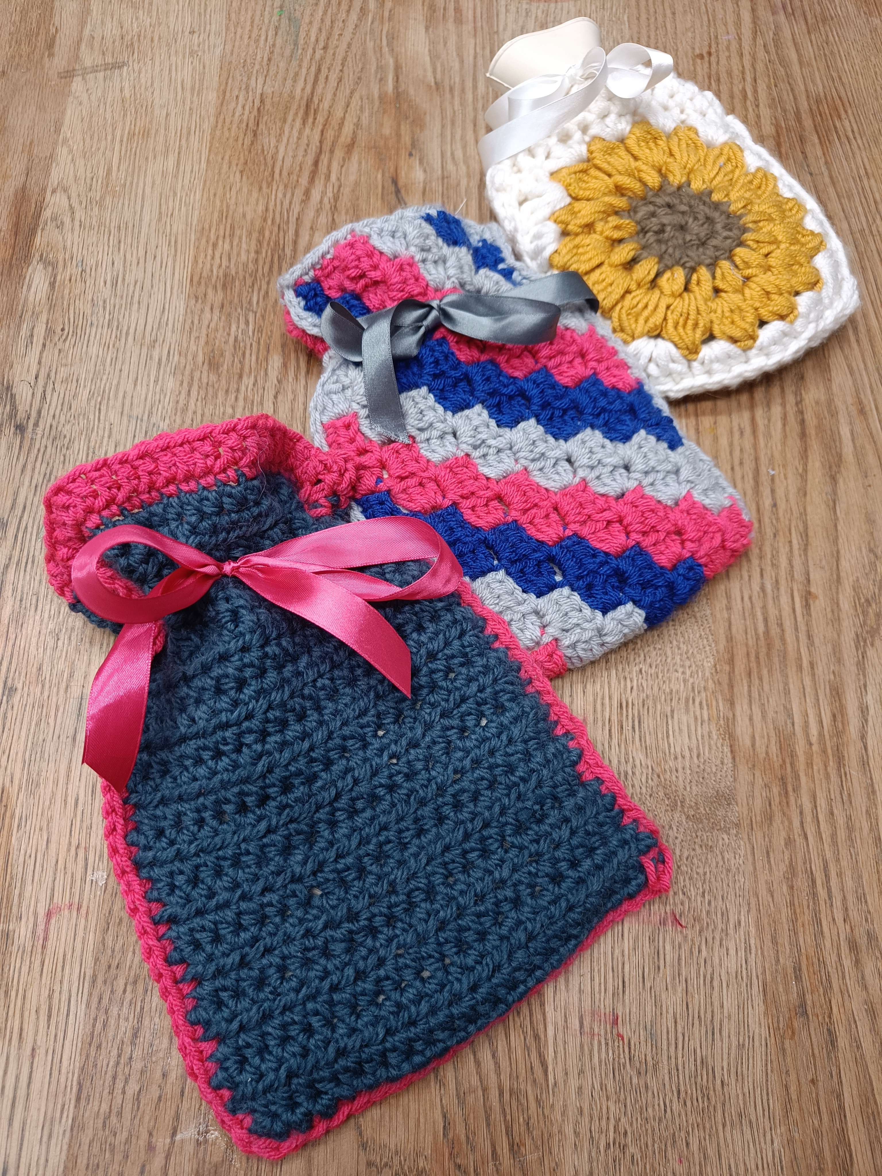 three handmade crochet hot water bottle covers lined up on a wooden table