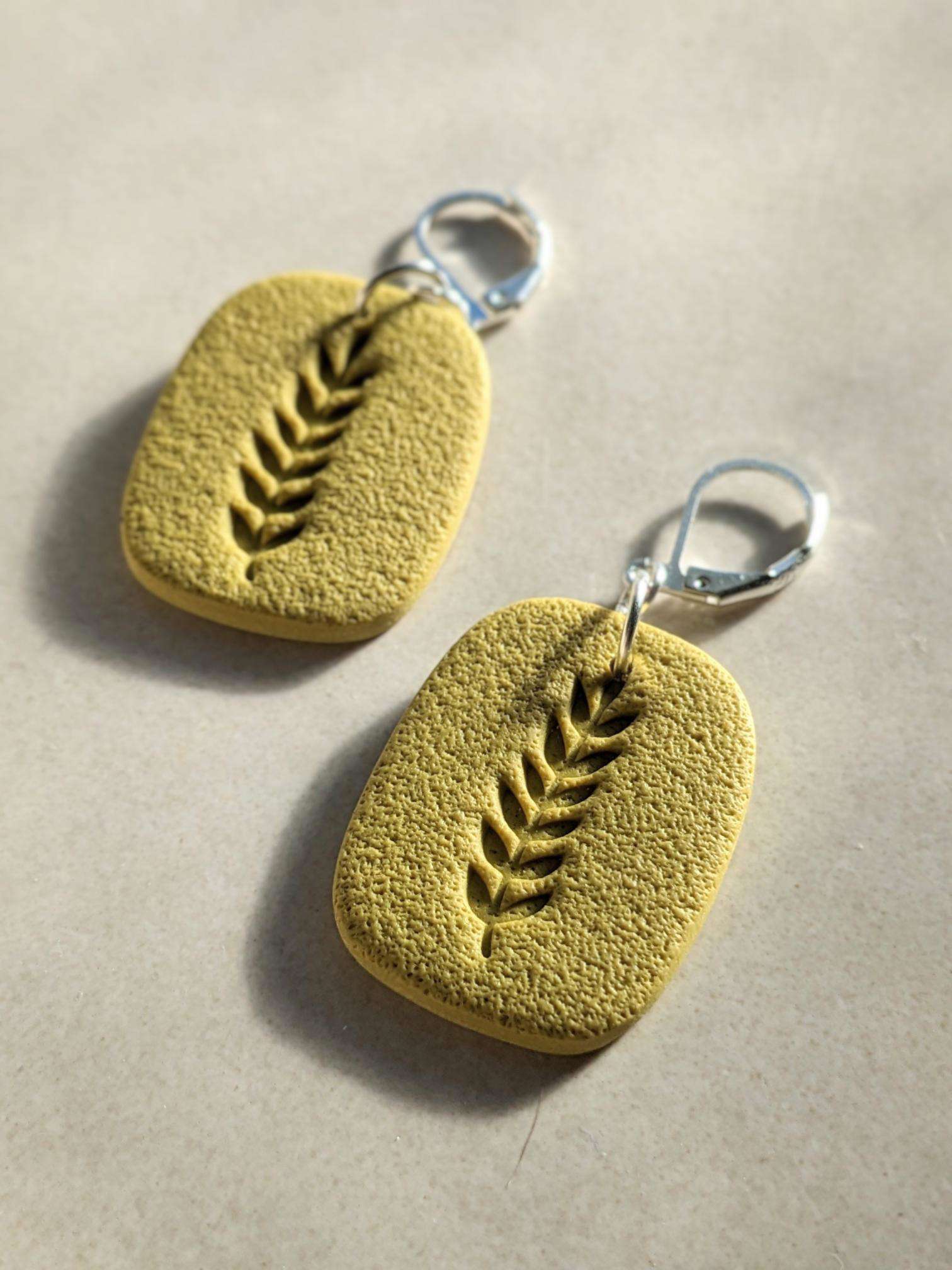 a pair of handmade yellow polymer earrings with small leaf imprints made by Gemma Forde