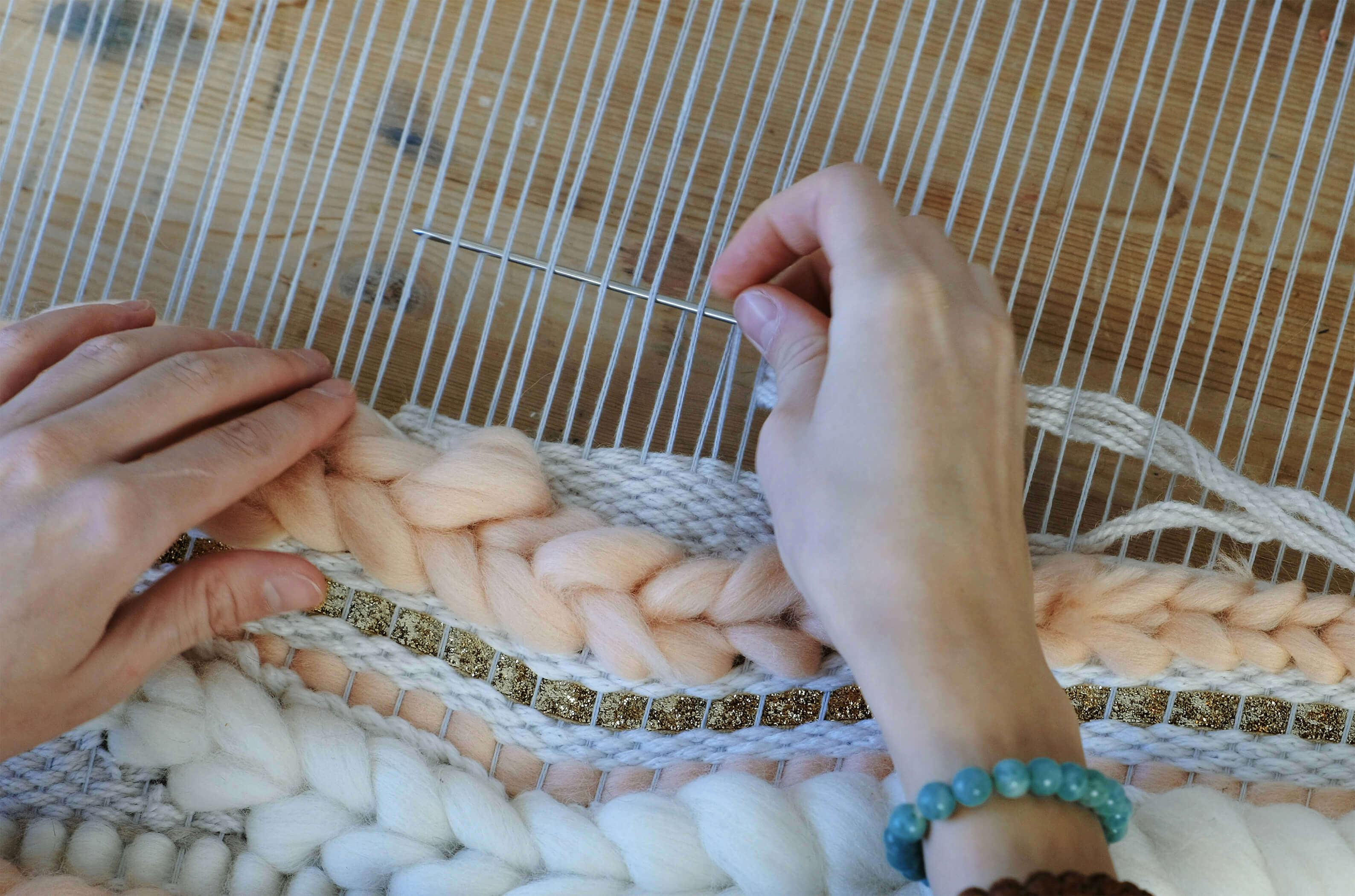 A hand using a loom and yarn needle to weave a yarn piece