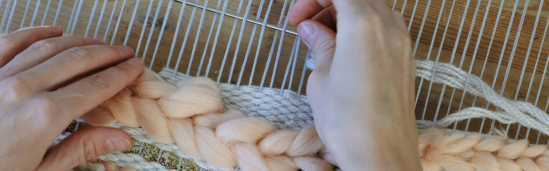 A hand using a loom and yarn needle to weave a yarn piece