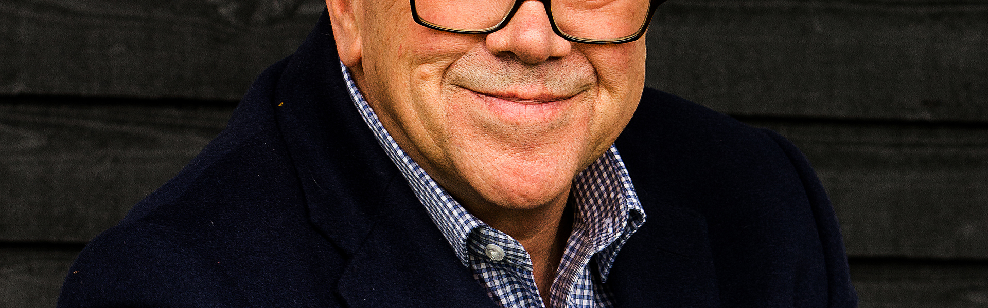 Main Image: a photo of cosy crime author Simon Brett, wearing a navy suit jacket, smiling at the camera.