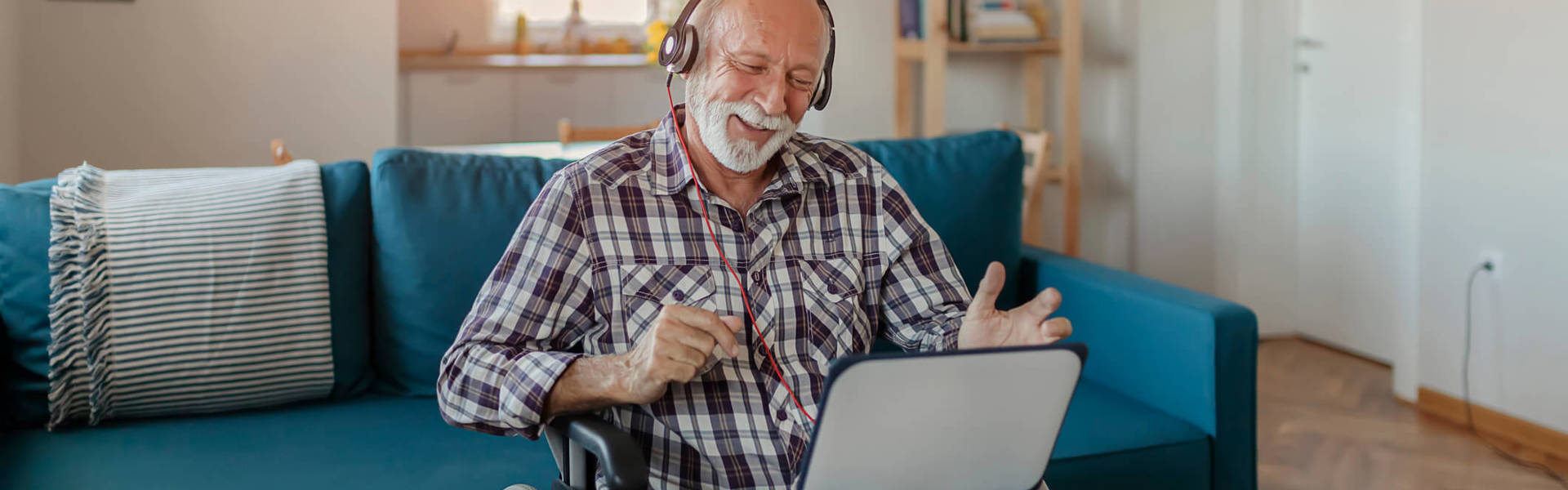 a man in a wheelchair wearing headphones and laughing whilst watching a laptop