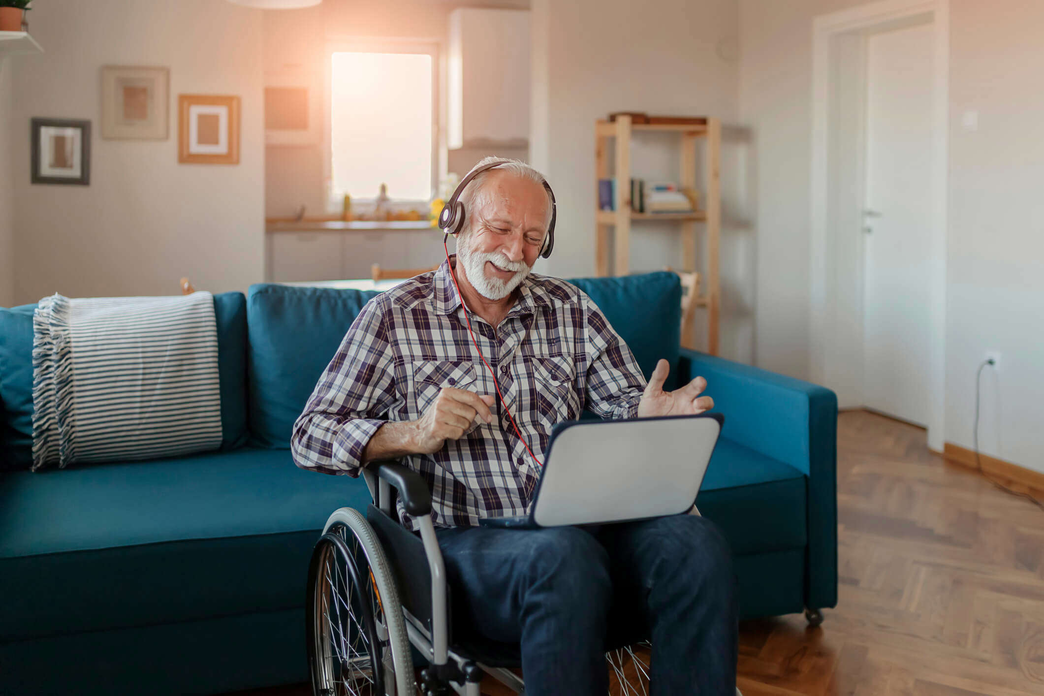 a man in a wheelchair wearing headphones and laughing whilst watching a laptop