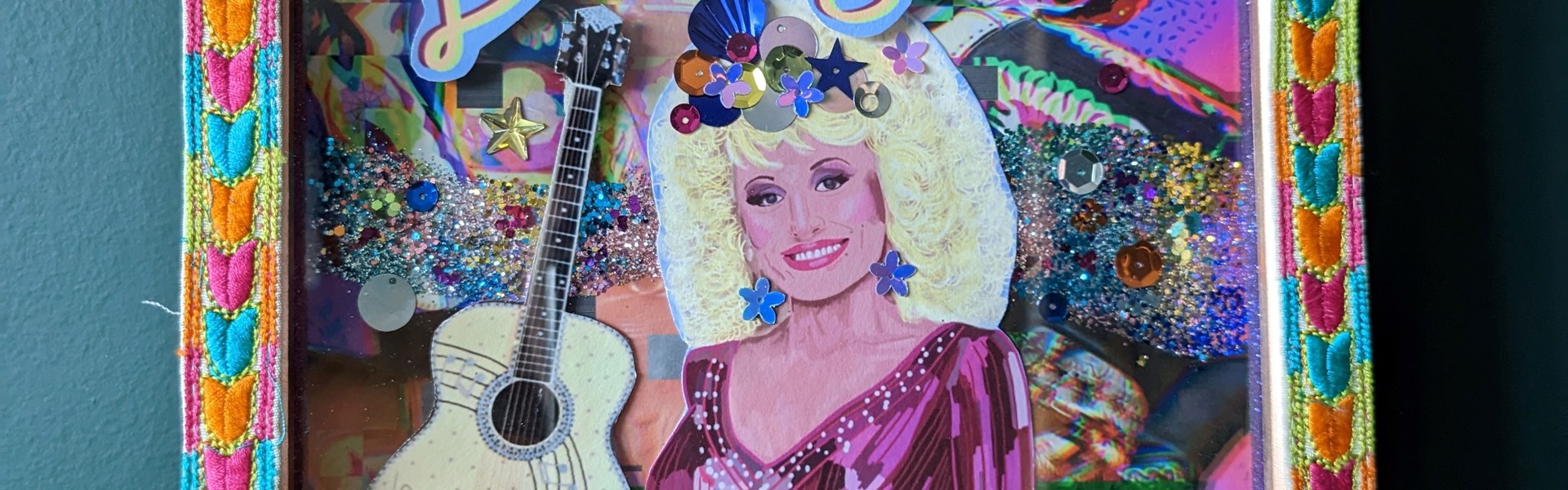 Multi-coloured shadow box shrine made with a variety of materials displaying a paper image of the singer Dolly Parton with the word "Dolly" displayed to the left of her