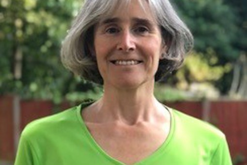 Headshot photo of Lidia Lonergan, Parkinson’s and FLexercise exercise and movement Instructor, from Live Well Exercise, outside in a bright green FLexercise t-shirt.