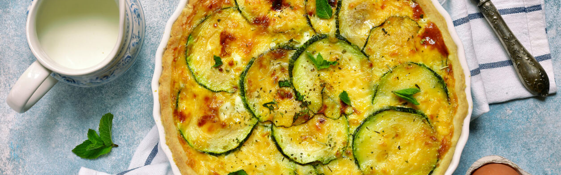 Mediterranean vegetables and hash brown quiche in an oven dish, on a towel with ingredients around it.