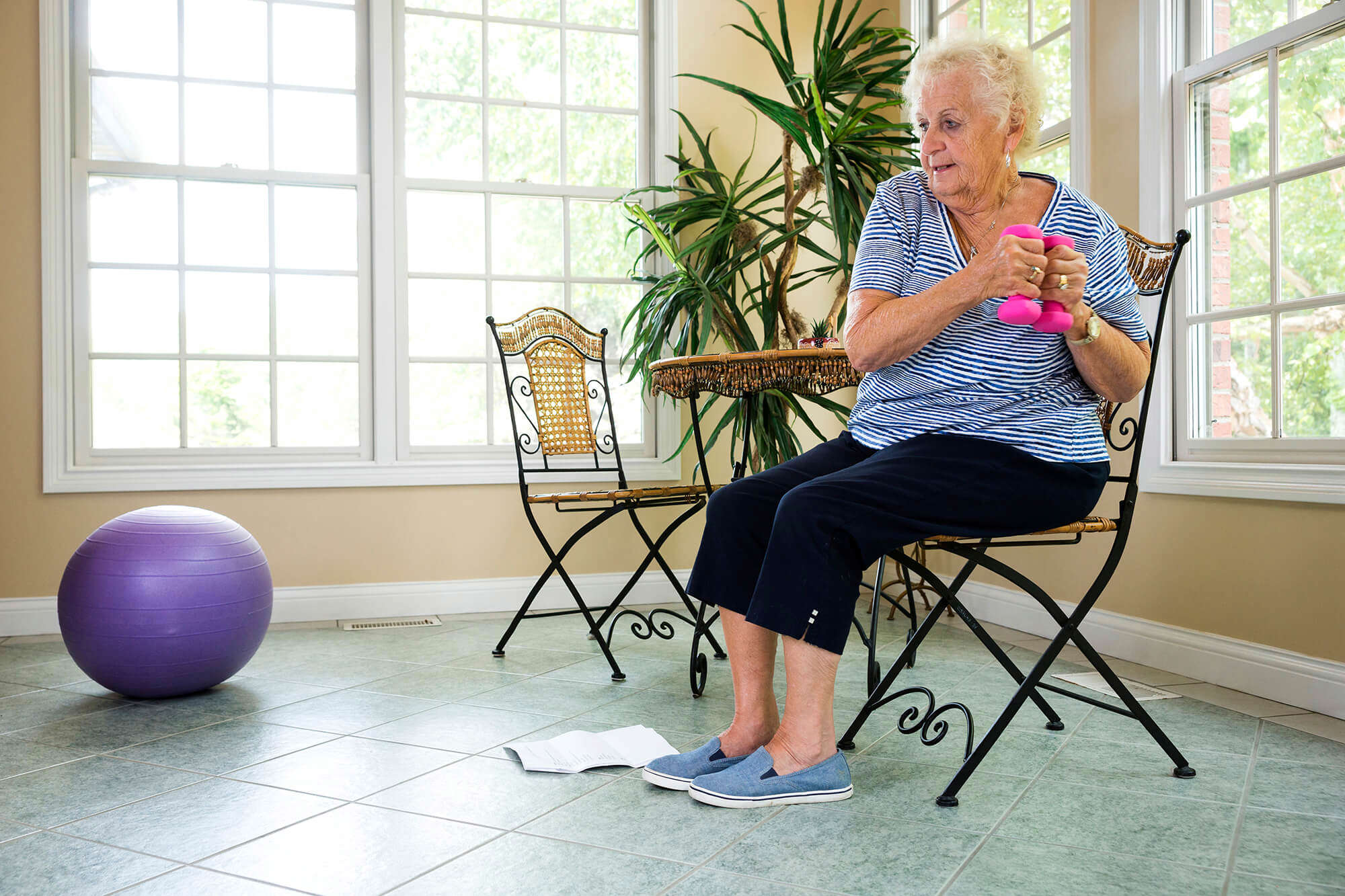 An older woman doing seated exercises while sitting on a chair and using weights 