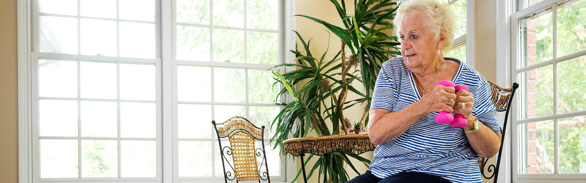 An older woman doing seated exercises while sitting on a chair and using weights