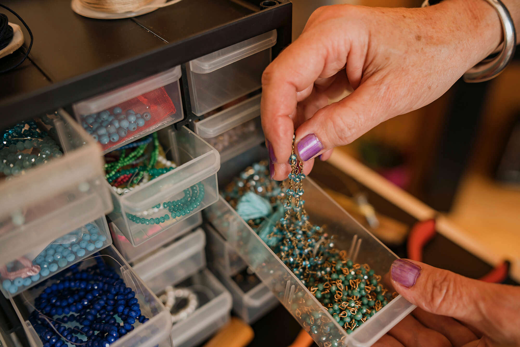 A hand reaching into a bead station with an assortment of drawers full of coloured beads