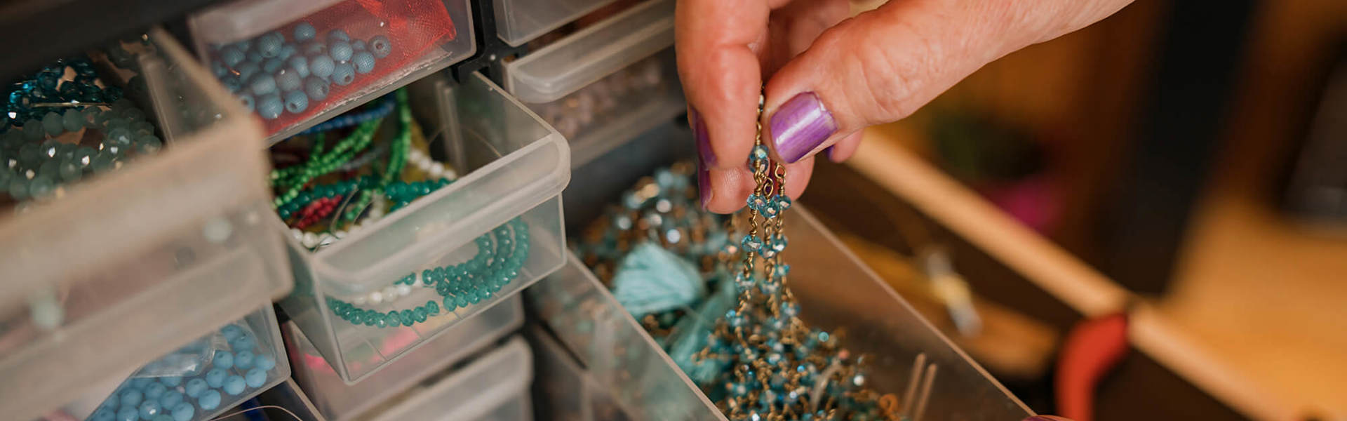 A hand reaching into a bead station with an assortment of drawers full of coloured beads