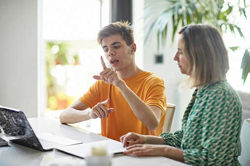 a woman and a boy learning sign language from a laptop