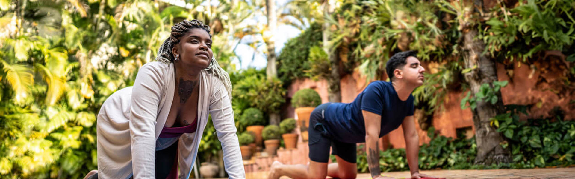 A woman and a man in cat cow position whilst doing yoga outdoors in the garden