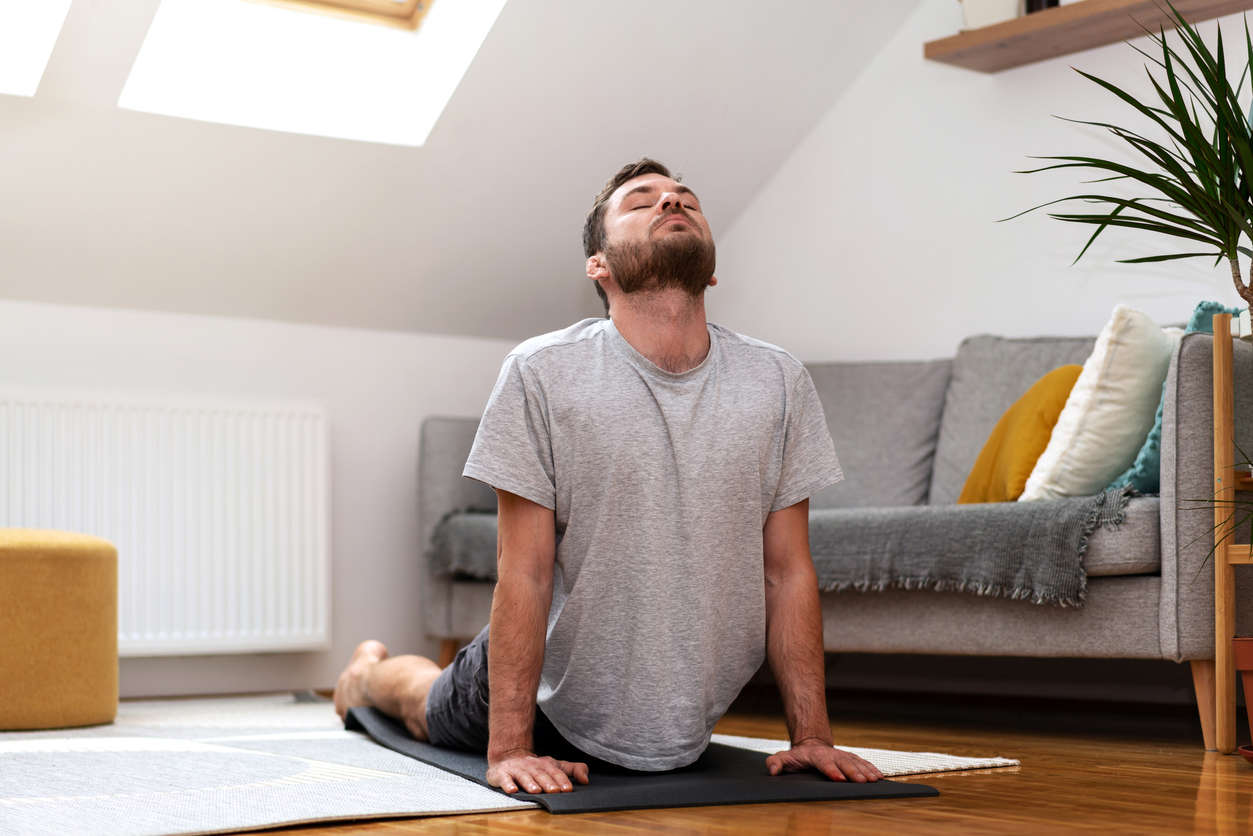 A young man doing yoga t home in the living room in cobra position