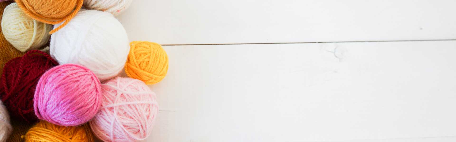 multicoloured balls of yarn on a white wooden background