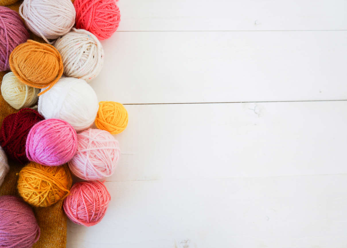 multicoloured balls of yarn on a white wooden background