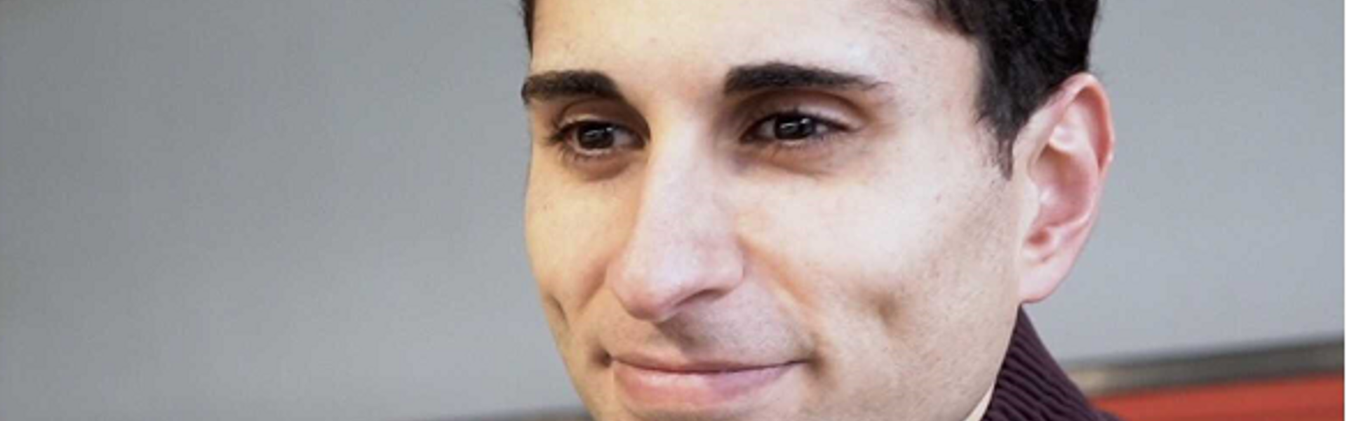 Head shot photo of Dr Hussain smiling, wearing a brow jacket.