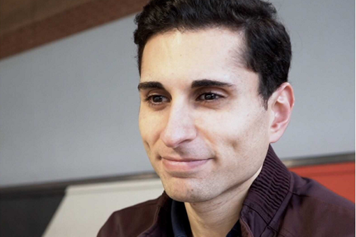 Head shot photo of Dr Hussain smiling, wearing a brow jacket.