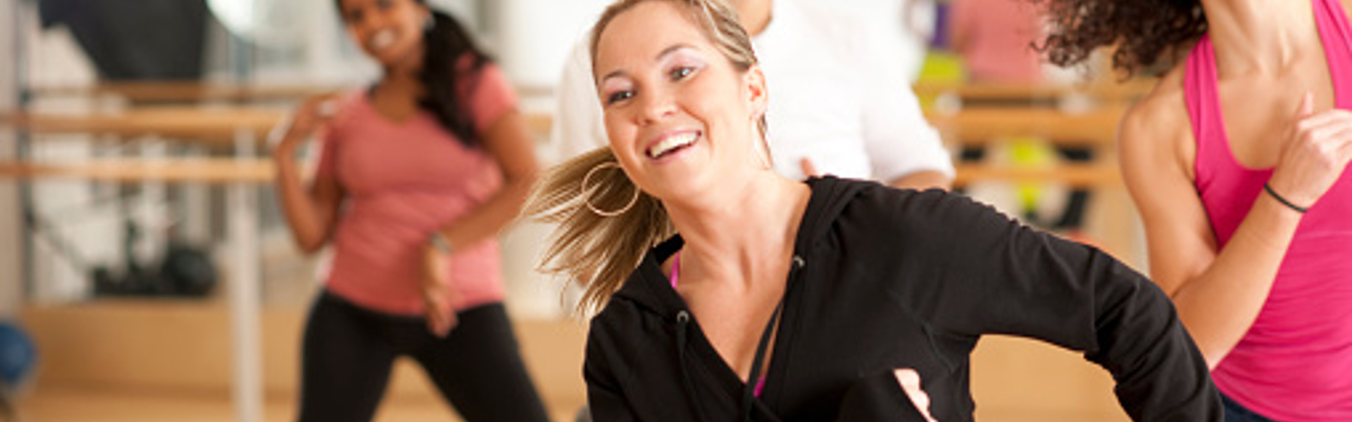 A woman wearing workout clothes dancing at a Zumba class and smiling