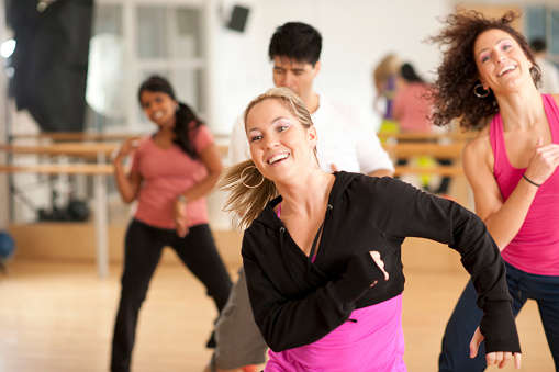 A woman wearing workout clothes dancing at a Zumba class and smiling