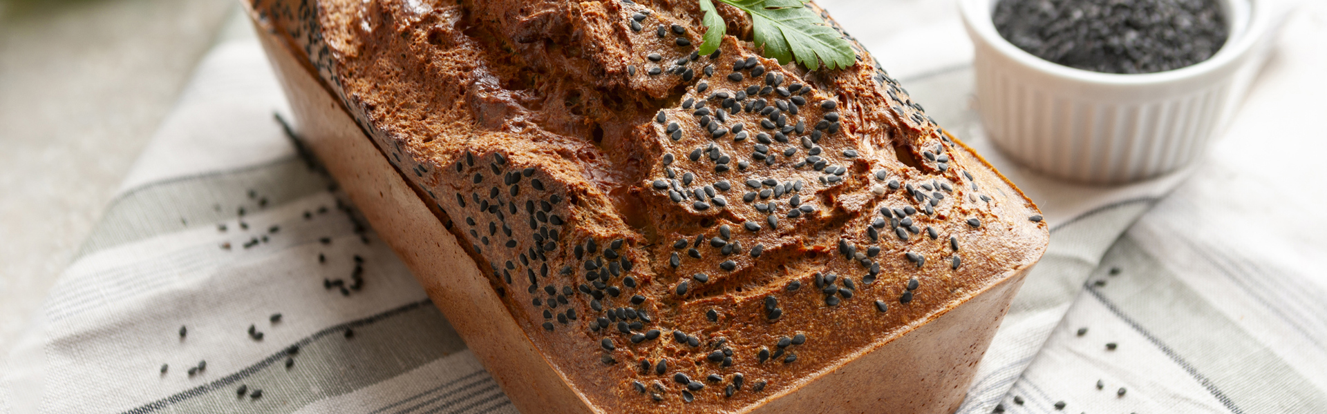 Main image: a gluten-free red lentil bread loaf, with black sesame seeds on top and a parsley sprig on top.