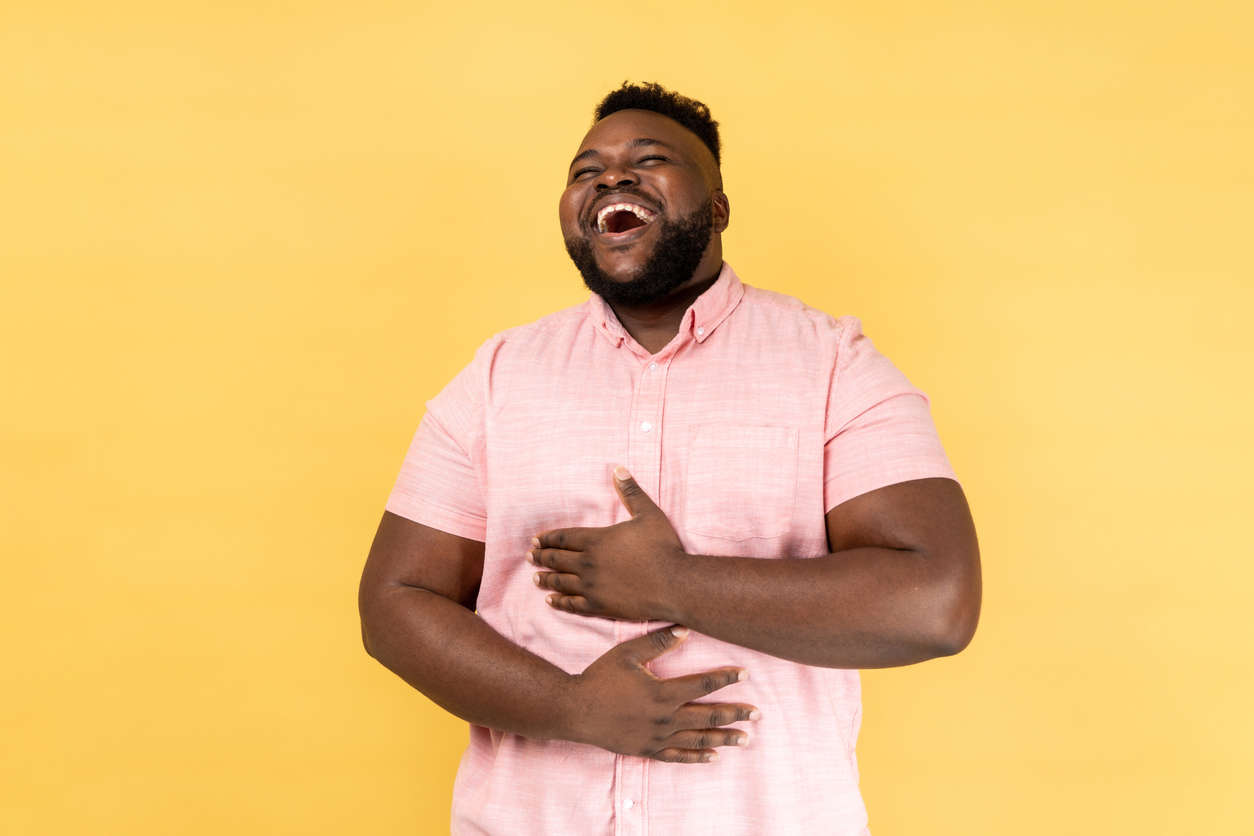 a man wearing a pink shirt laughing with a yellow background