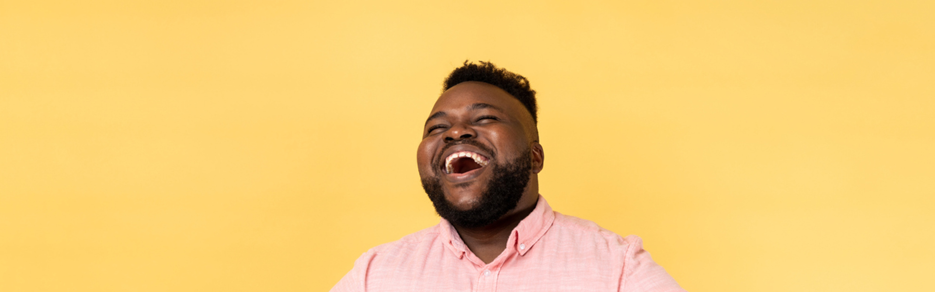 a man wearing a pink shirt laughing with a yellow background