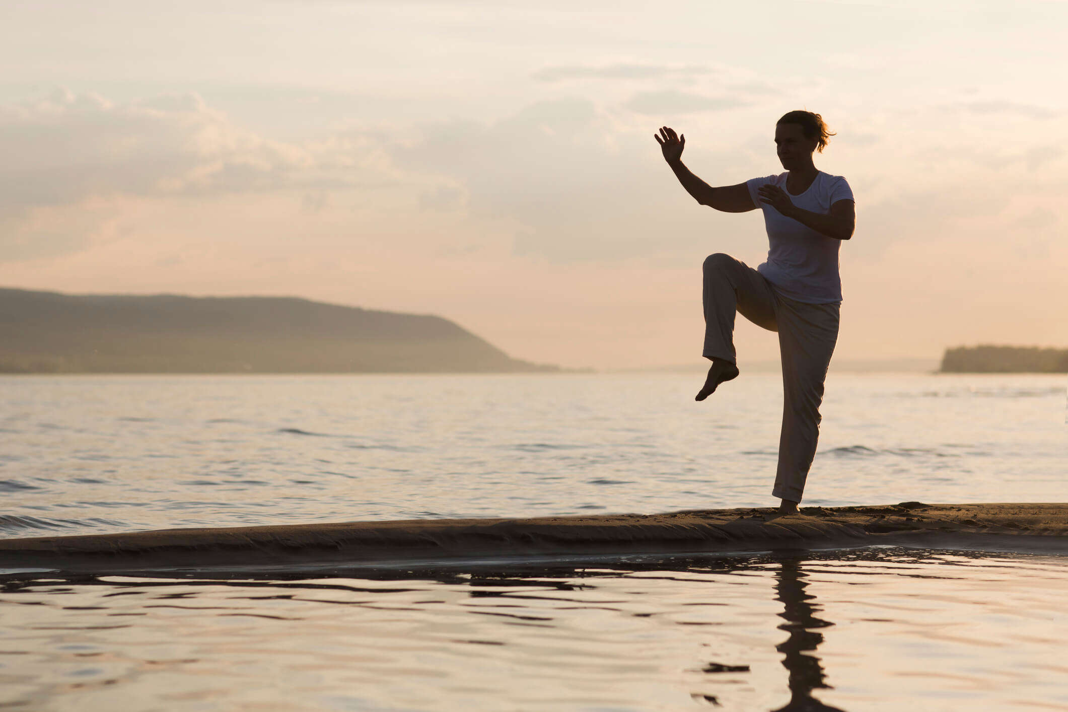 a silhouette of someone doing Qi Gong on the beach at sunset