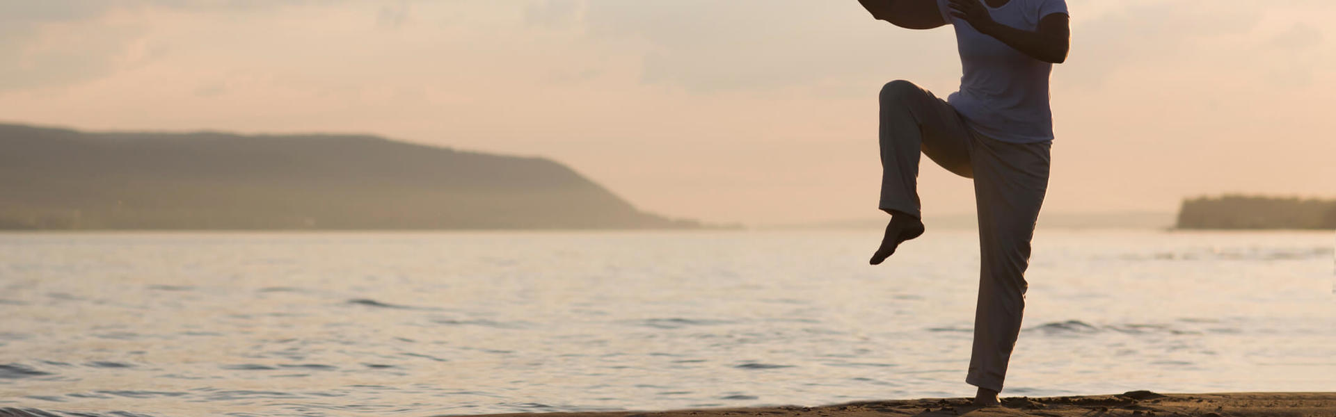 a silhouette of someone doing Qi Gong on the beach at sunset