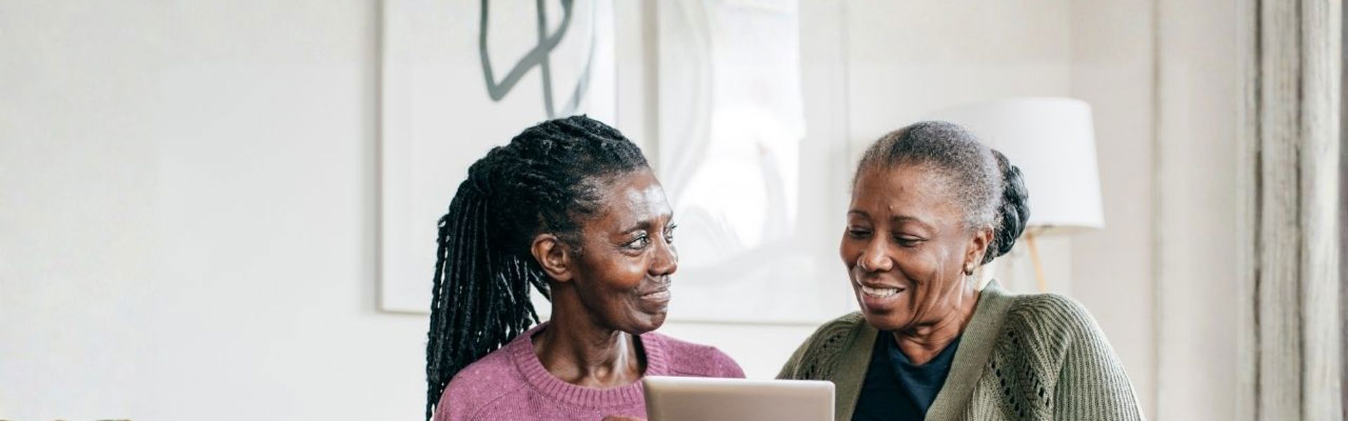 A mother and daughter sat on the sofa together looking through dementia resources on a tablet together.